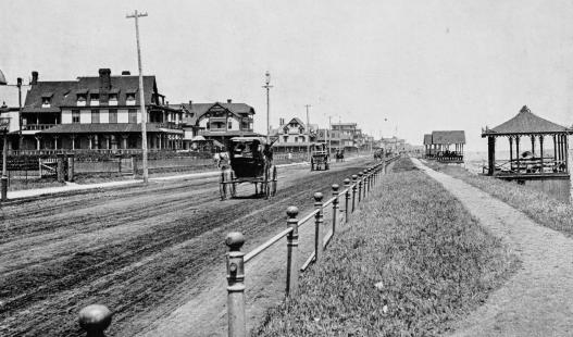 Black and white image of a town with dirt road with early aged automobiles