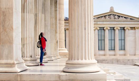 A young teenage girl looks up at the ceiling beneath the columns of the Athenian Academy in Athens, Greece.