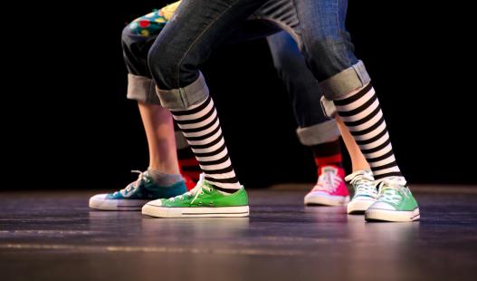 A close-up of the feet of three hip-hop dancers on stage, wearing colorful sneakers.