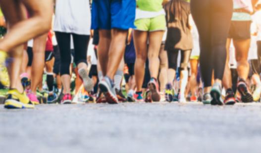 The legs of a couple dozen walkers participating in a race, with pavement featured prominently in the foreground.