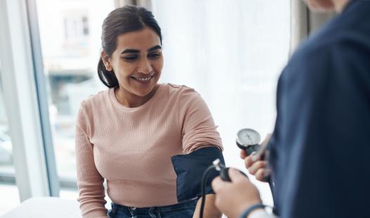 Woman in pink shirt getting blood pressure checked by a medical professional.
