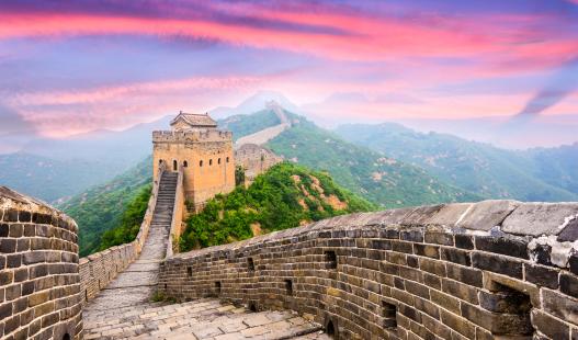 View of China's Great Wall, with a pink sky and mountains behind it.