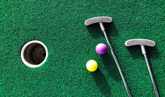 birds eye view of two miniature golf clubs, two balls, and a hole on a mini golf course