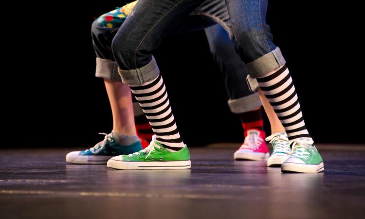 A close-up of the feet of three hip-hop dancers on stage, wearing colorful sneakers.