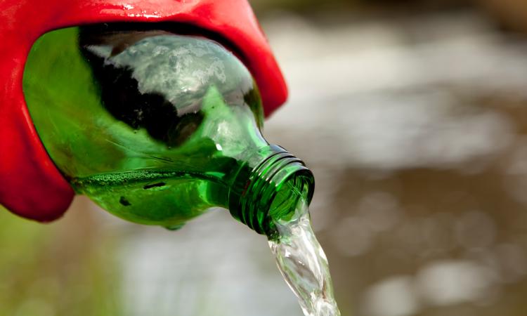 An environmental researcher wearing red rubber gloves pours water out of a green bottle.