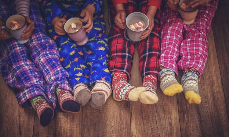 Four children's legs and feet in pajama pants, children holding mugs of hot chocolate in their laps